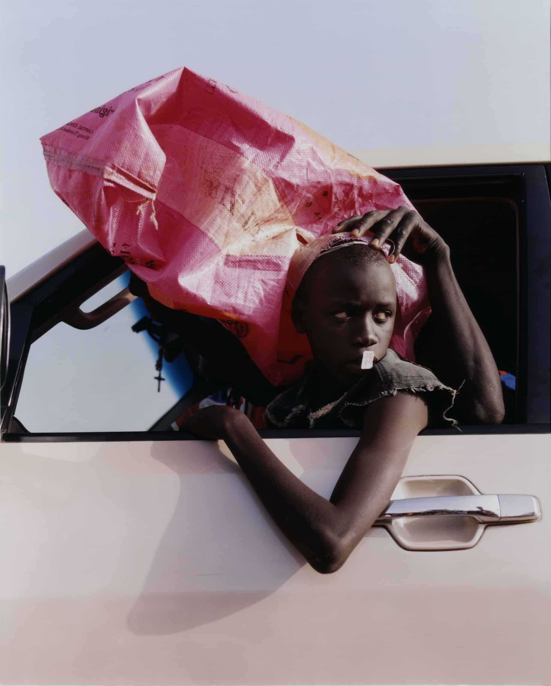 Enfant penché à la fenêtre d'une voiture, un sac rose vif posé sur le toit