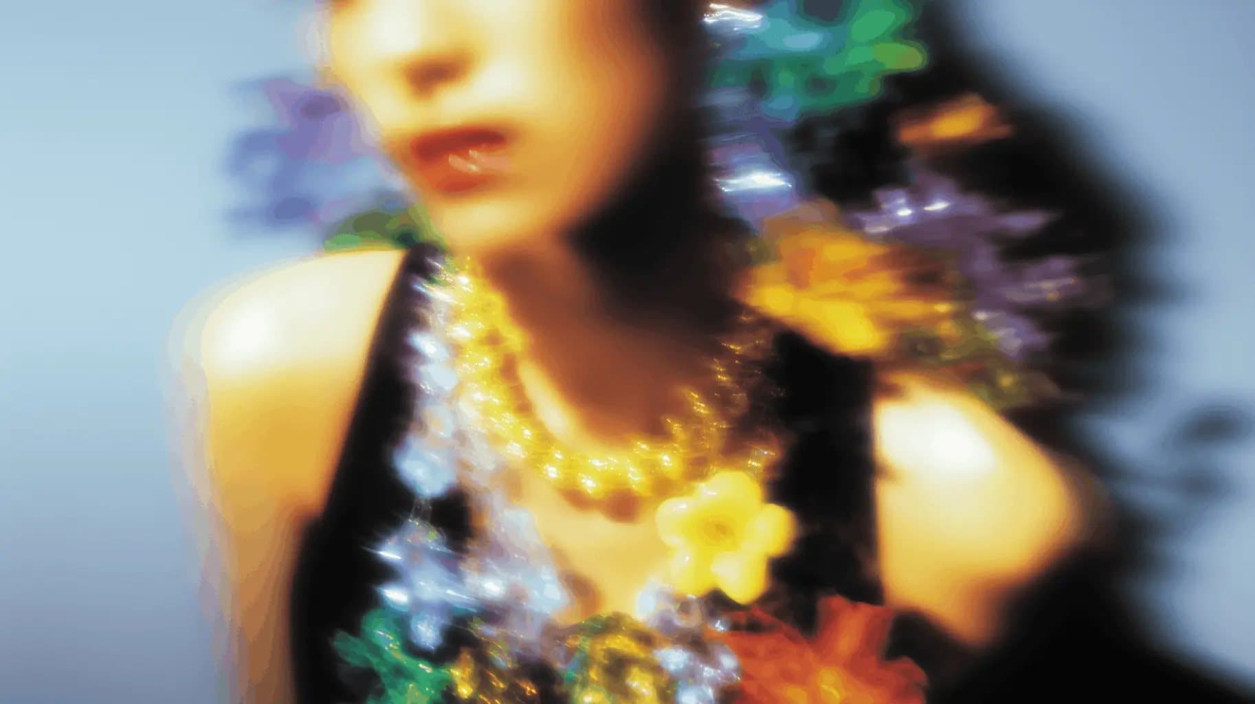 JILL key visual: a blurred, brightly coloured portrait with a yellow bead necklace and flowers in the foreground
