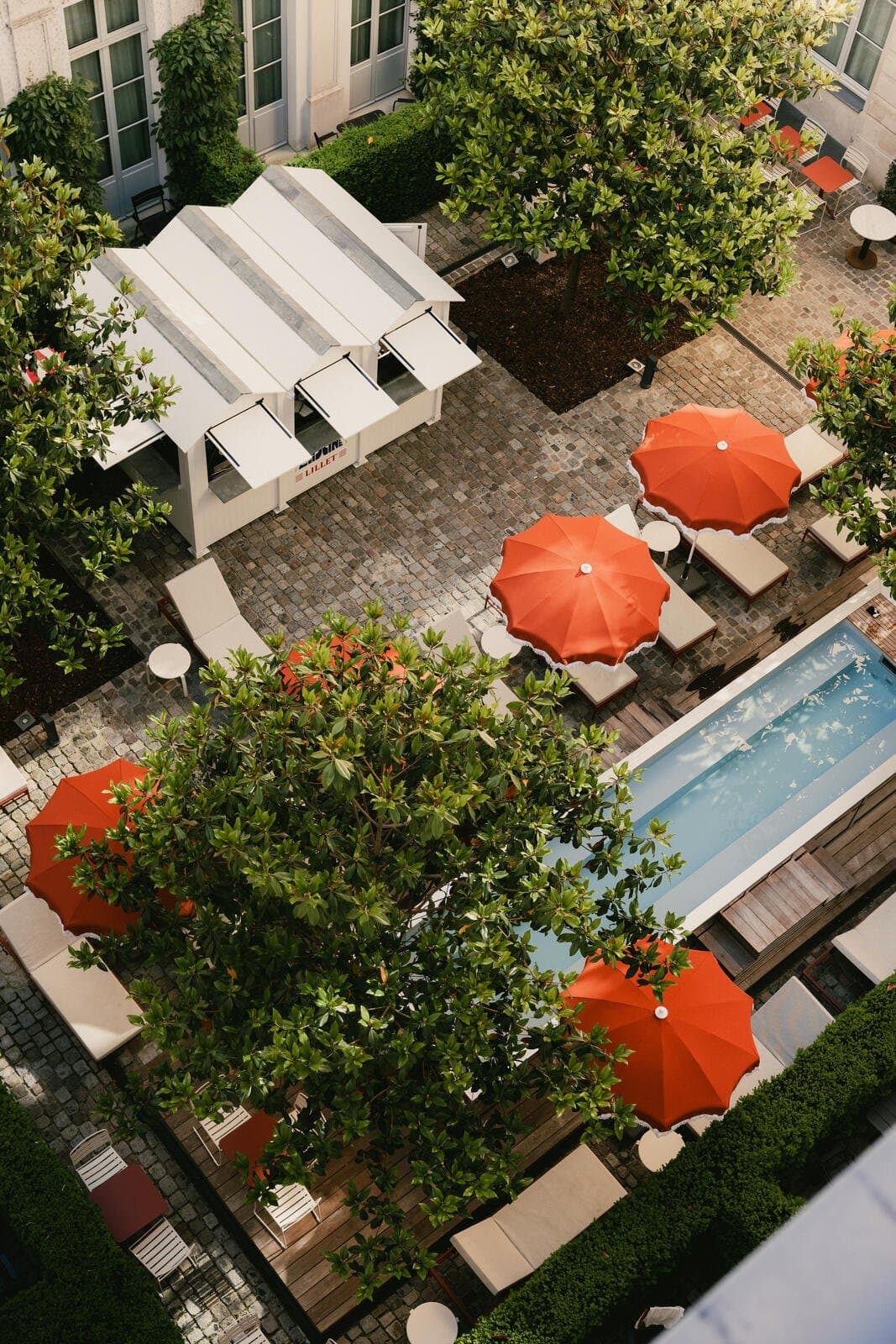 Vue plongeante sur le bassin éphémère et les parasols orange dans la cour pavée du Hoxton