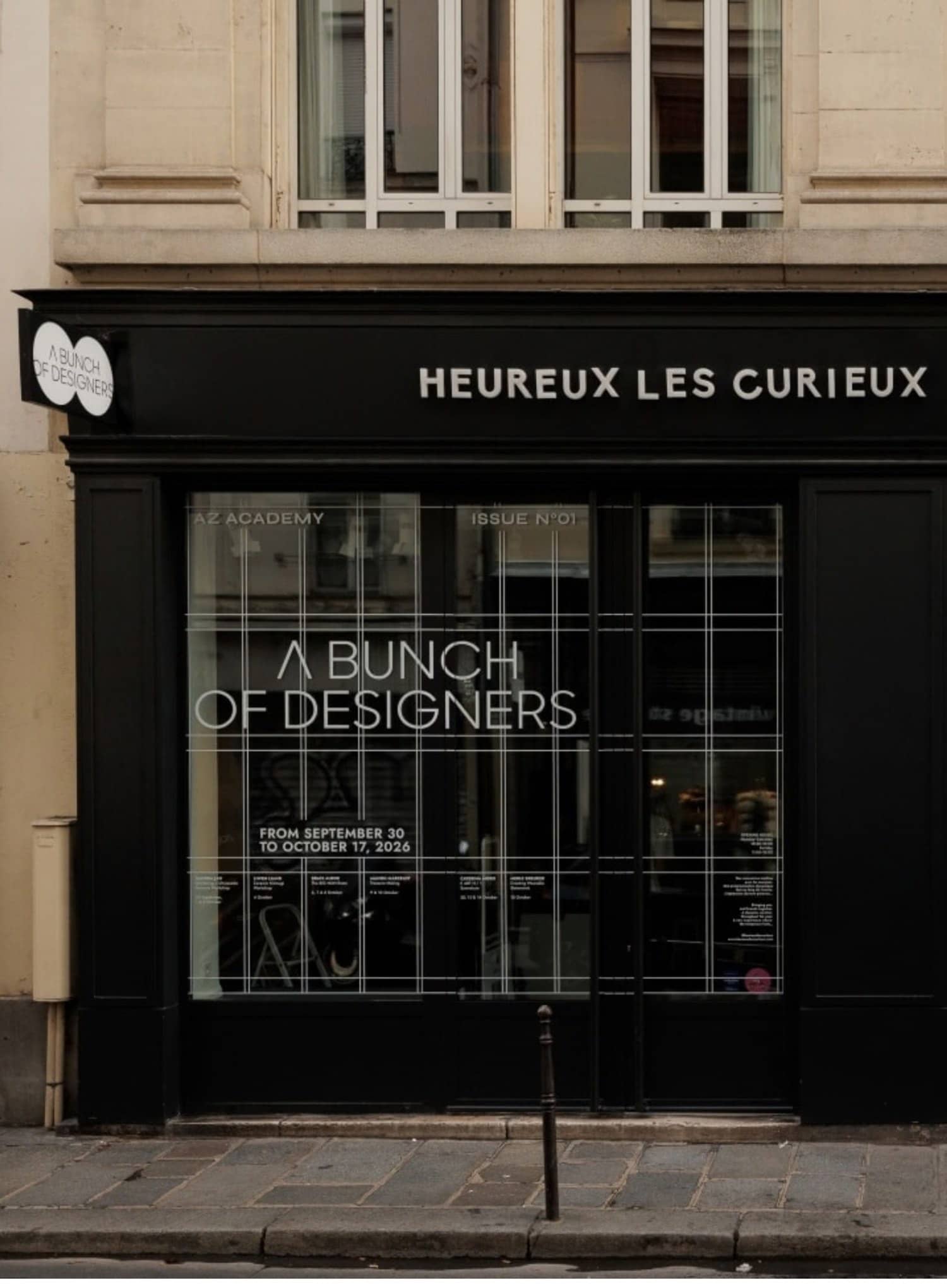 Devanture noire de Heureux les Curieux avec l'affiche A Bunch of Designers en vitrine, rue du Pont aux Choux