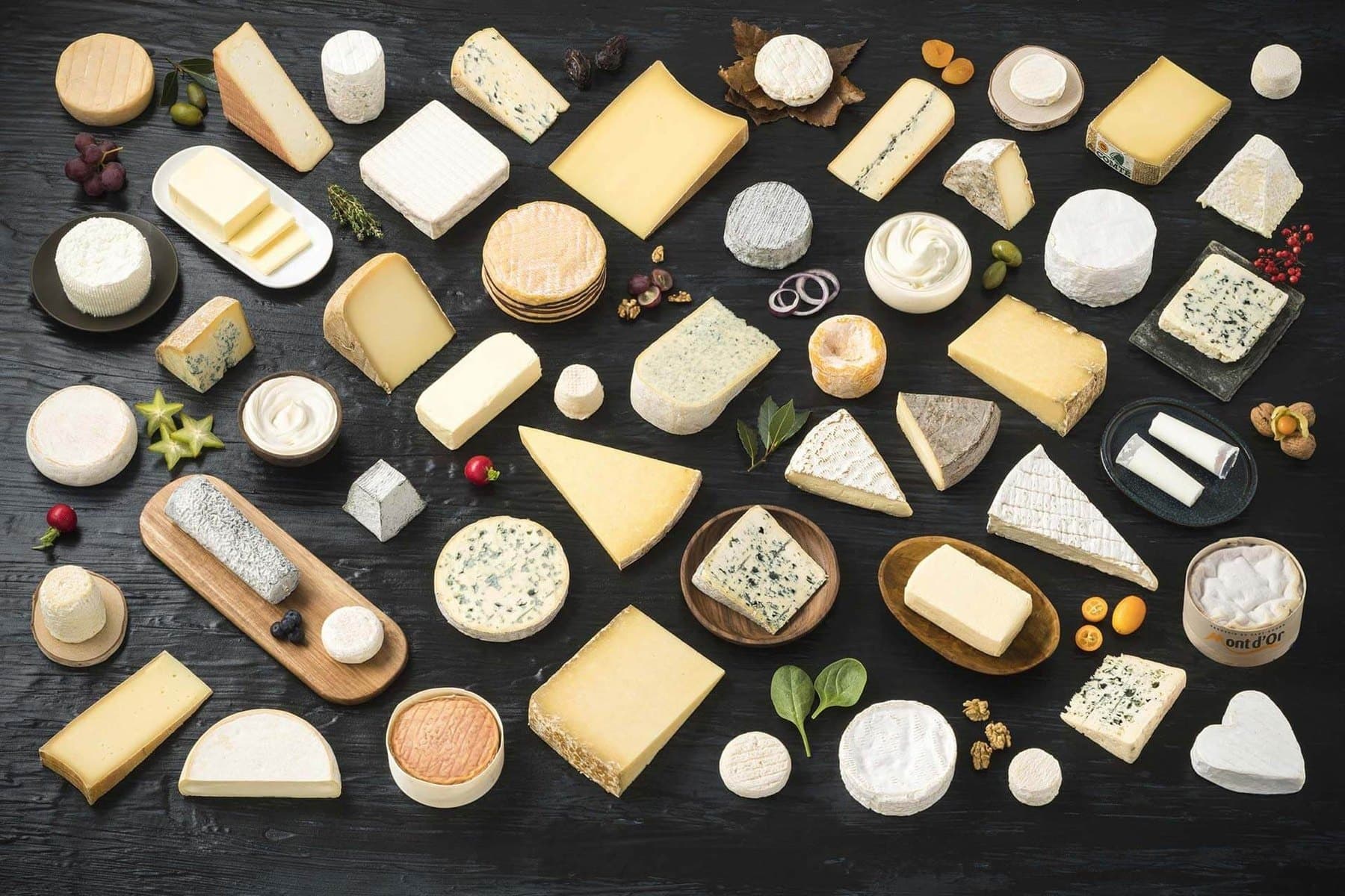 Les 52 produits laitiers AOP français disposés à plat sur un plateau de bois noir