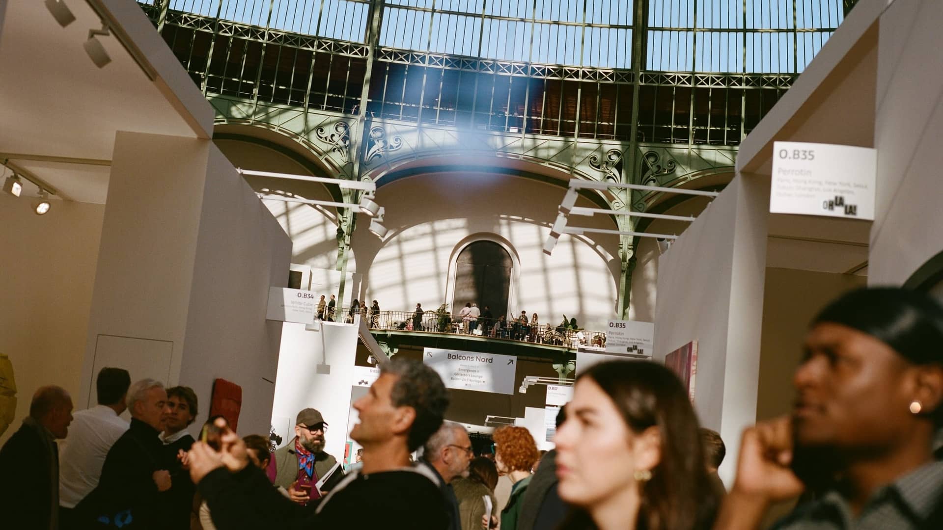 Visiteurs regardant les œuvres entre les stands d'Art Basel Paris sous la verrière du Grand Palais
