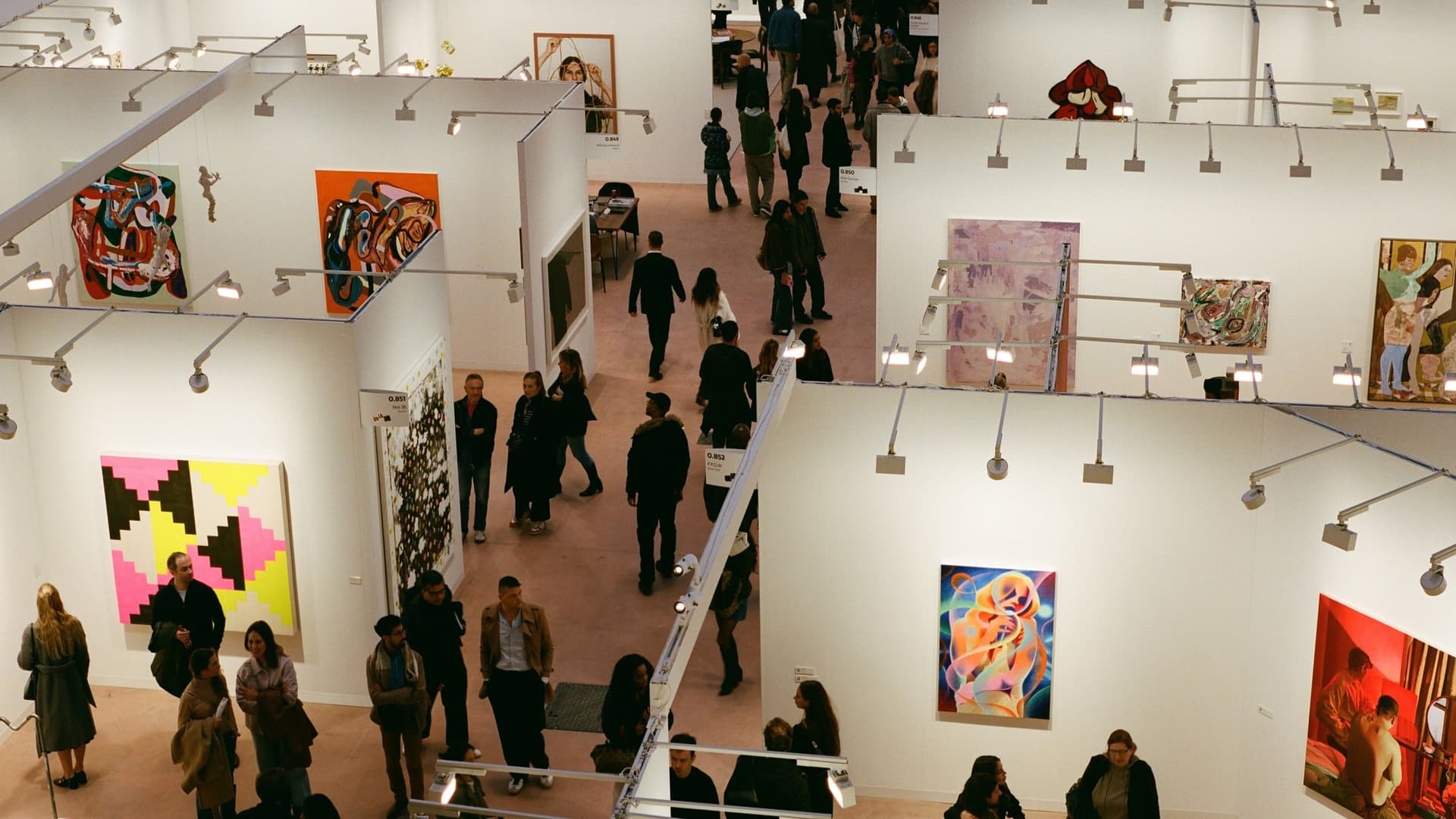 Vue plongeante sur les stands d'Art Basel Paris, toiles colorées accrochées aux cimaises et visiteurs dans les allées