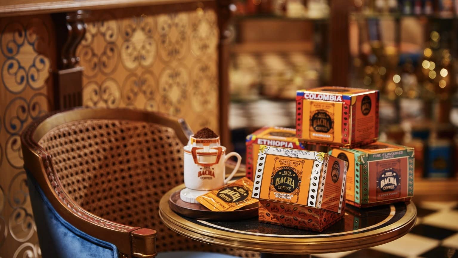 Coffrets Bacha Coffee orange posés sur un guéridon, fauteuil canné et sol en damier noir et blanc