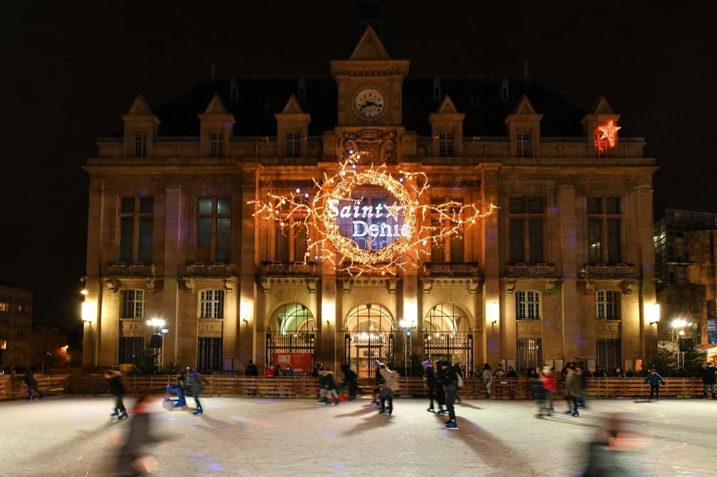 Patineurs devant l'hôtel de ville de Saint-Denis, sa façade décorée d'une couronne lumineuse pour Bel Hiver