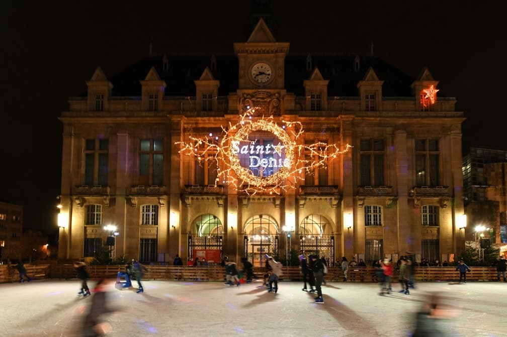 Patineurs devant l'hôtel de ville de Saint-Denis, sa façade décorée d'une couronne lumineuse pour Bel Hiver