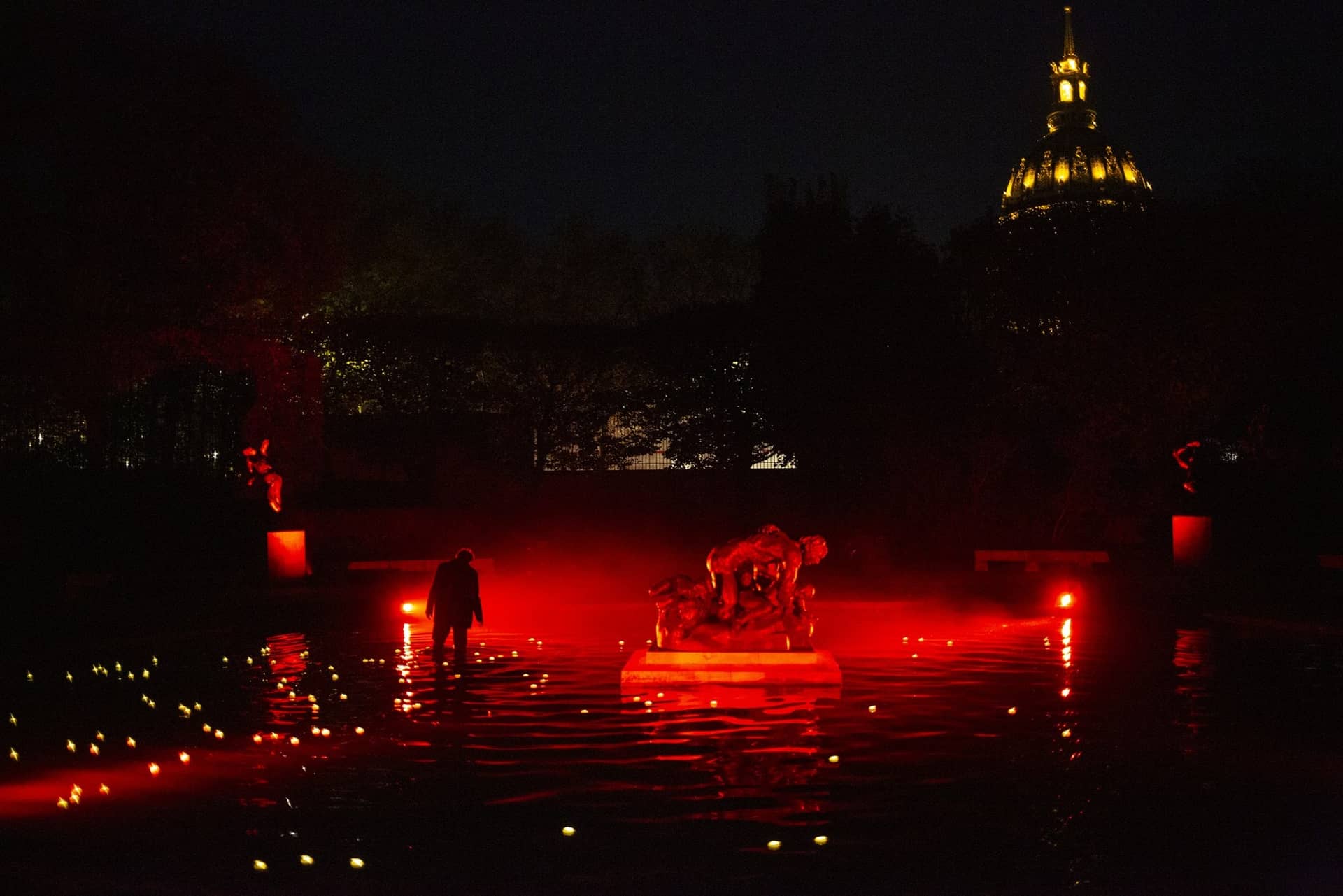 Le groupe d'Ugolin baigné de lumière rouge au milieu du bassin du musée Rodin, dôme des Invalides au fond