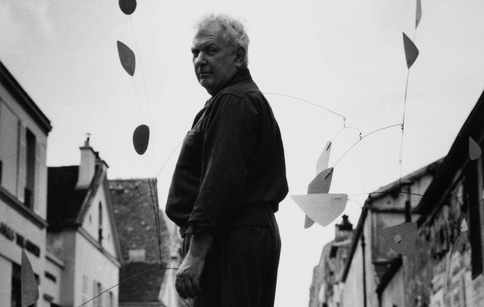 Alexander Calder en 1954 dans une rue de Paris, entouré d'un mobile aux formes noires et blanches, photo Agnès Varda