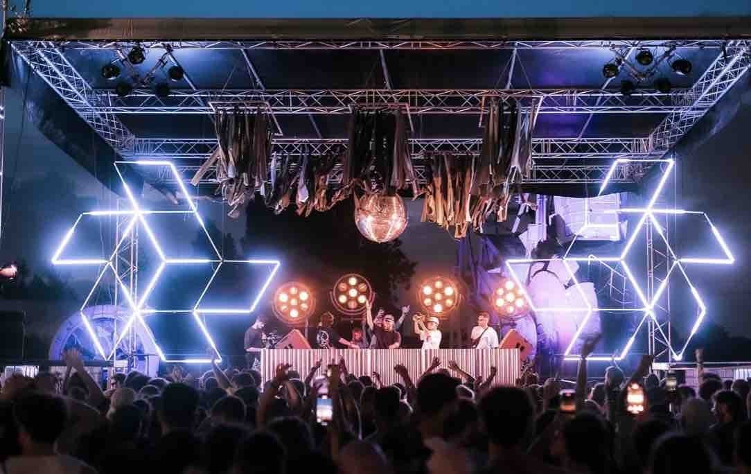 Foule bras levés devant une scène à néons hexagonaux et boule à facettes lors d'une soirée Chevry Agency