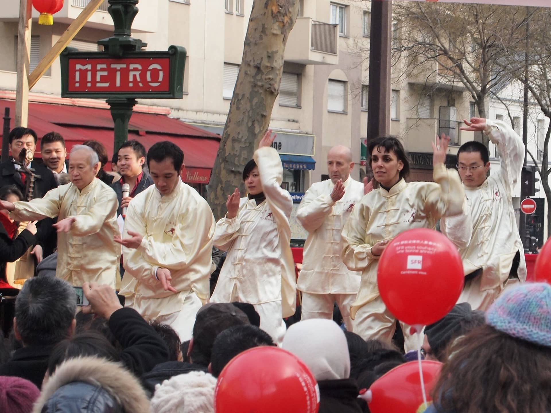 Danseurs en tenue blanche devant la bouche de métro Belleville, foule et ballons rouges