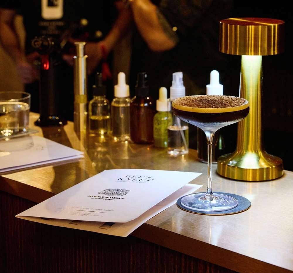 Coupe dorée posée sur un comptoir en inox, cocktail Bee's Knees coiffé de poudre