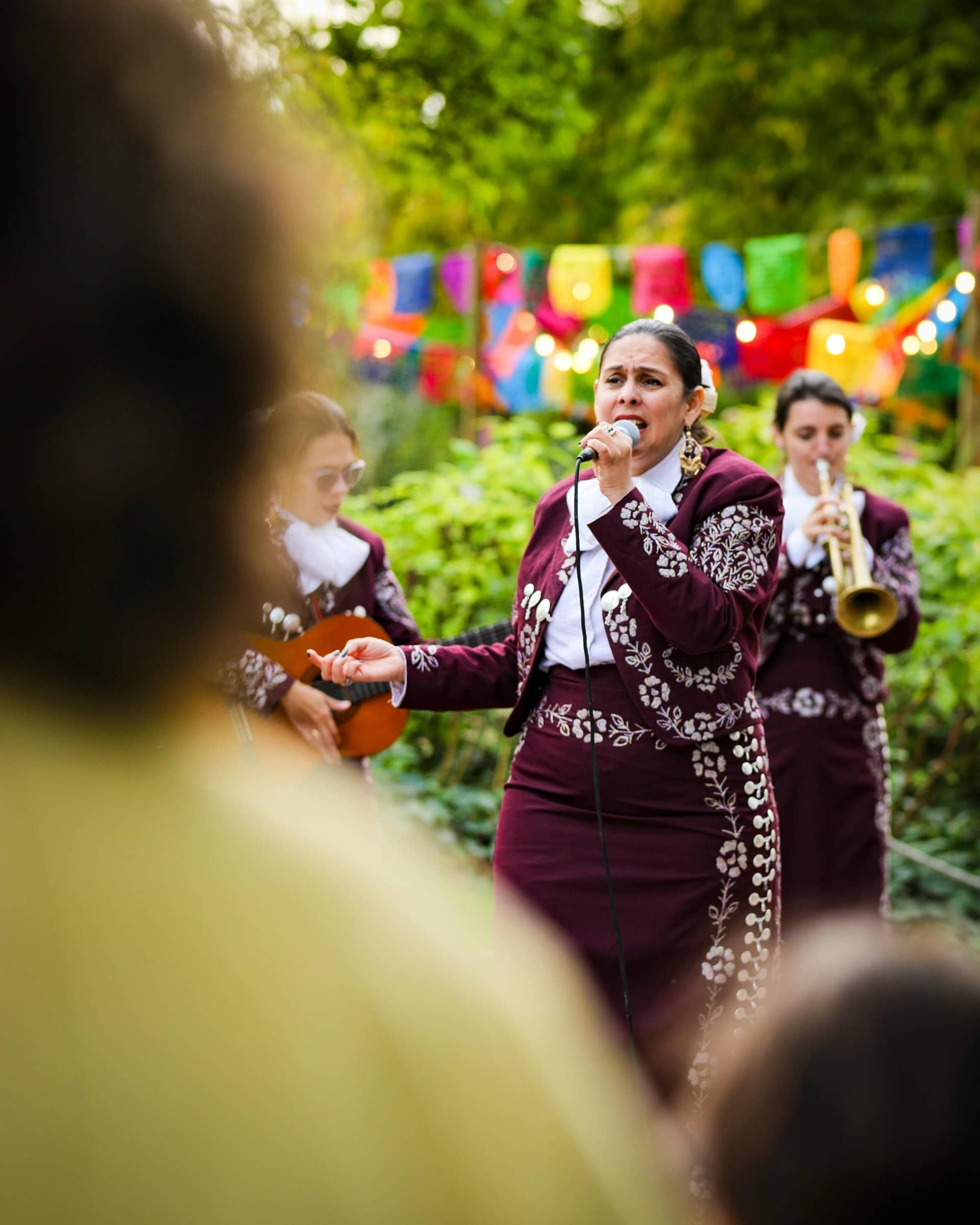 Mariachis en costume brodé qui chantent sous des guirlandes de papel picado au Jardin d'Acclimatation