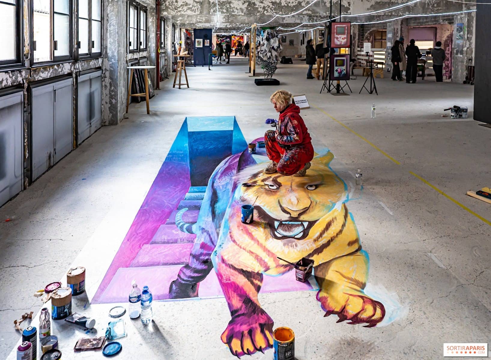 Une artiste peint au sol un tigre en trompe-l'œil violet et jaune, lors de l'édition 2025 de l'Expo des 150