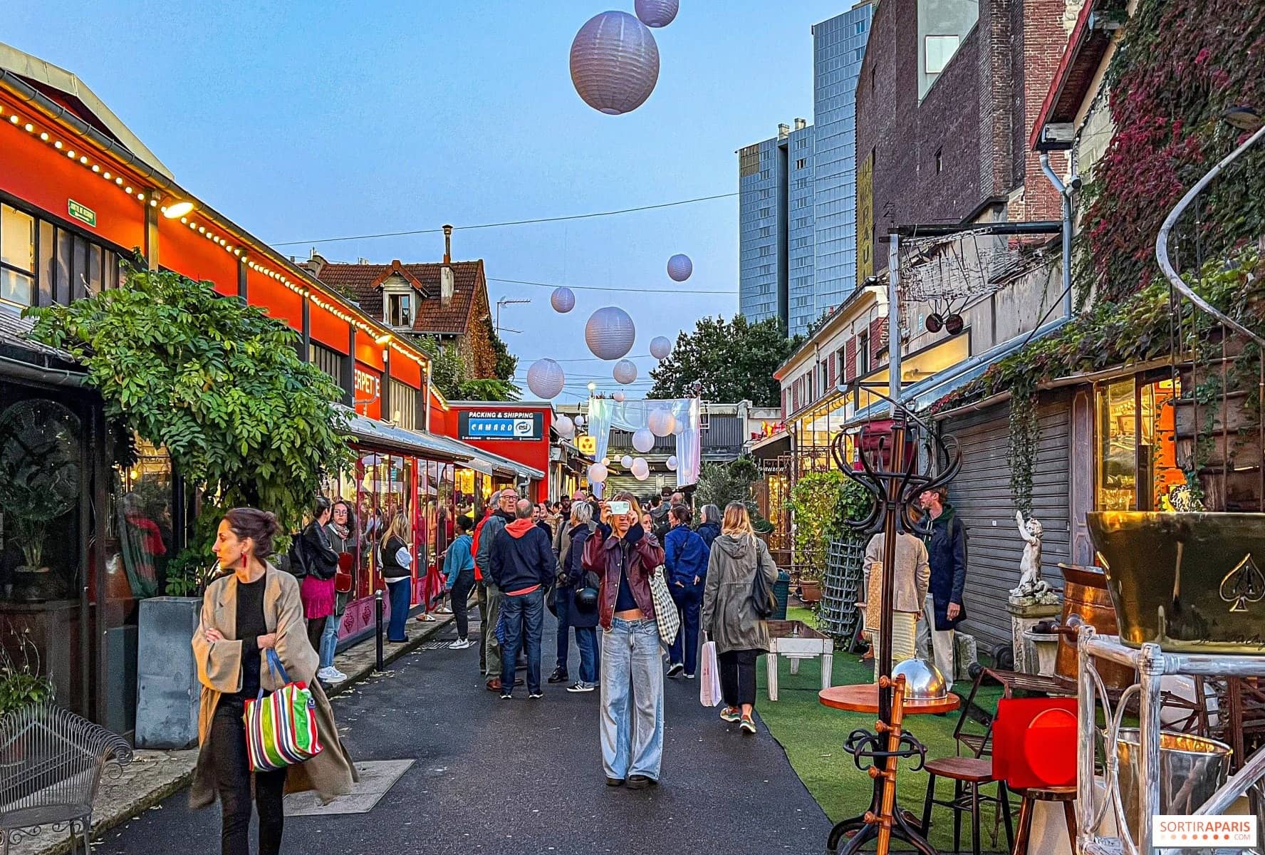 Des chineurs remontent une allée des Puces bordée de boutiques d'antiquaires ouvertes