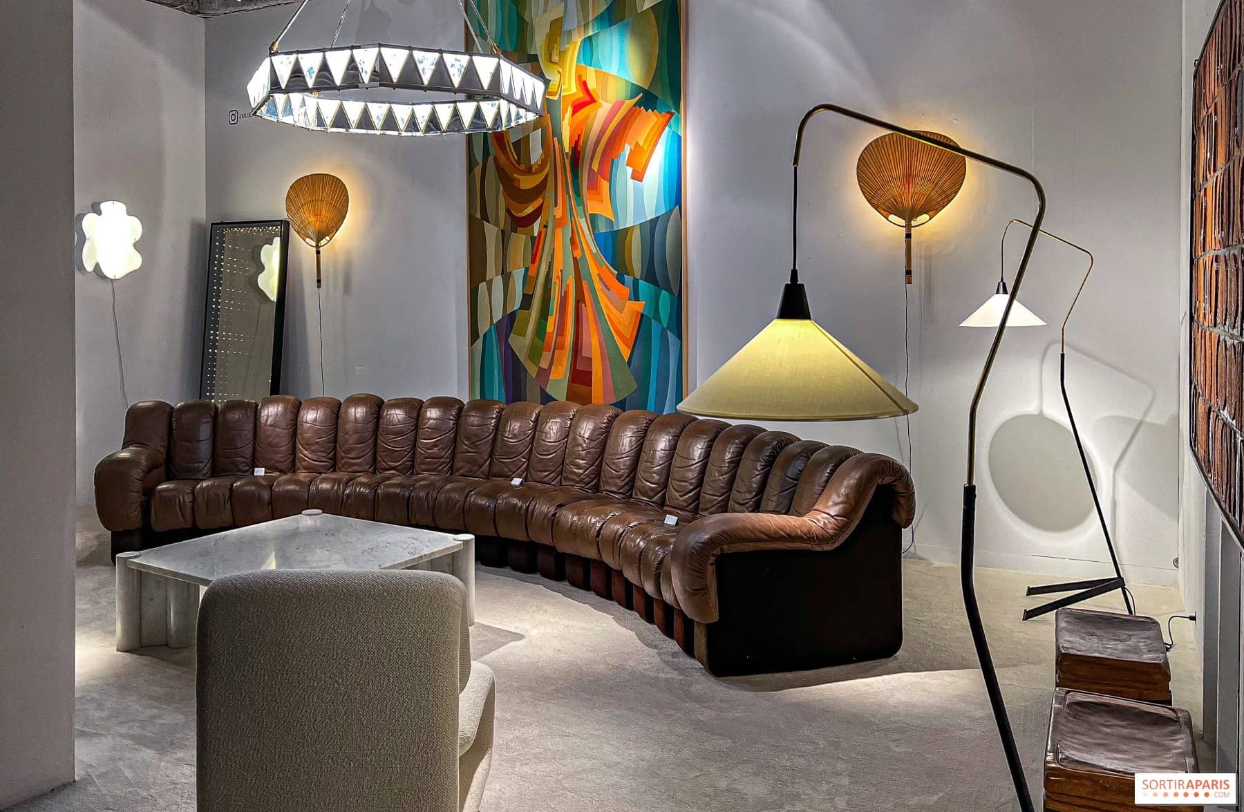 Canapé en cuir brun à modules courbes et lampadaires design dans un stand des Puces