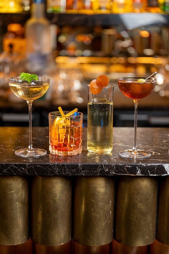 Trois cocktails ambrés posés sur le comptoir en marbre du bar du Publicisdrugstore, lors de l'édition 2025