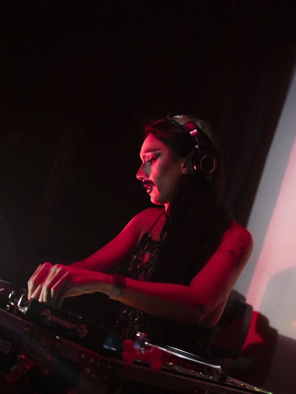 Artiste drag aux platines, casque sur les oreilles, dans une lumière rouge à la GenderFvck Klub