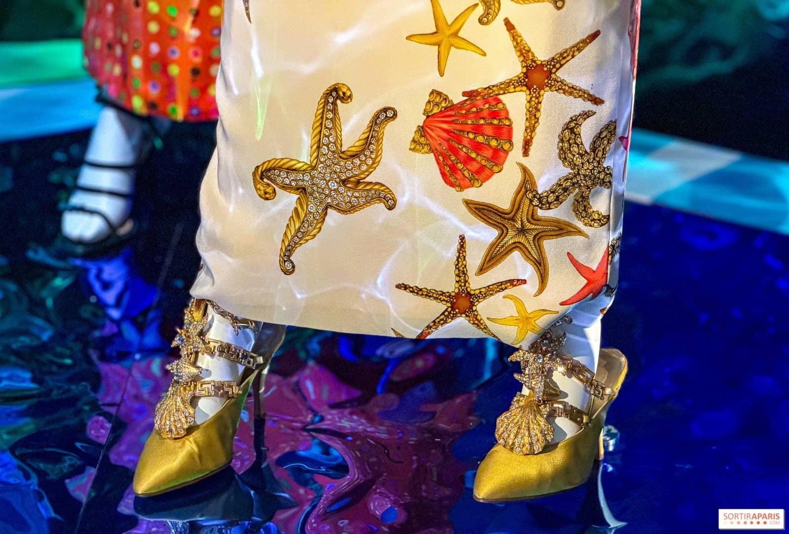 Robe brodée d'étoiles de mer et escarpins dorés devant un fond bleu électrique