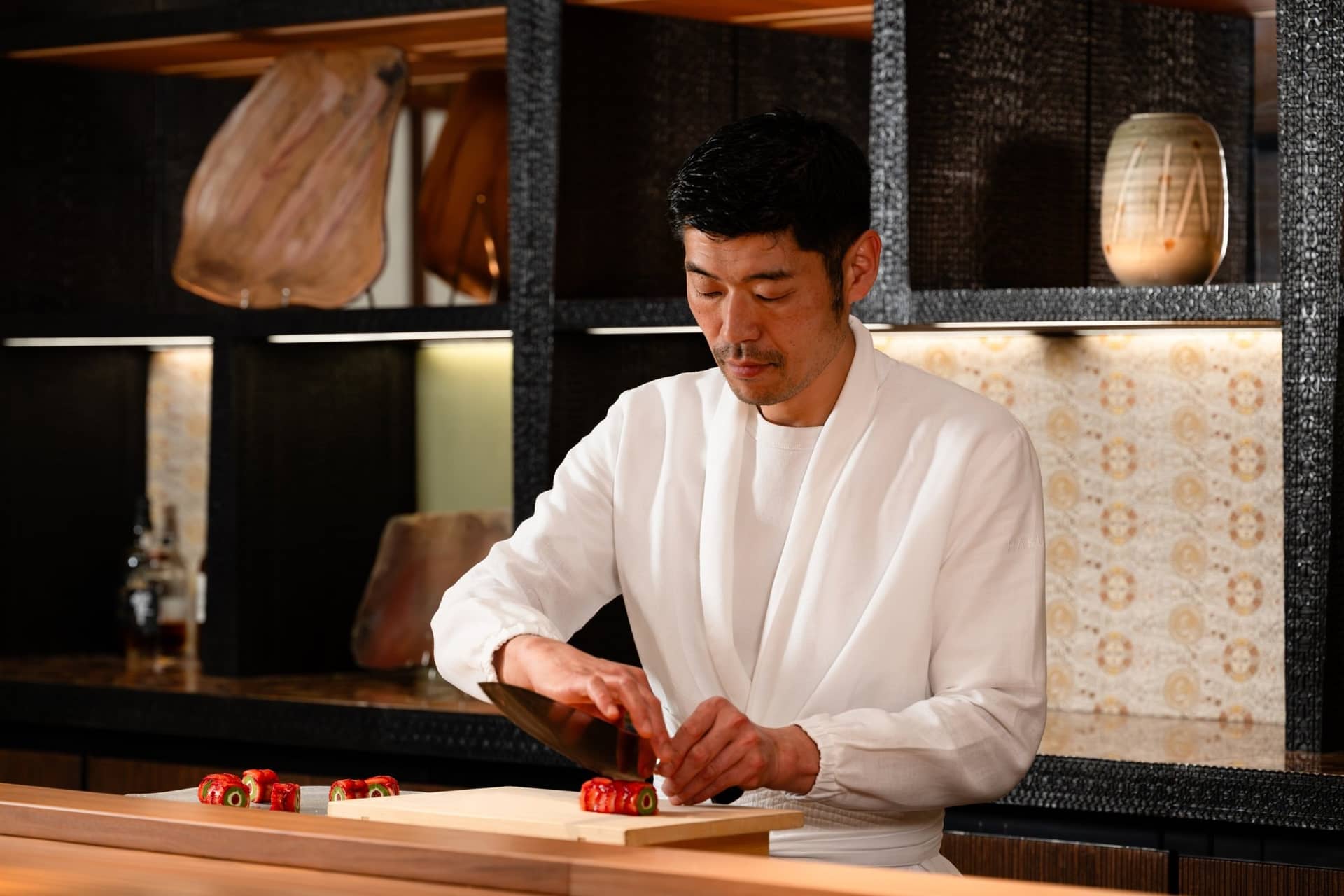 Un chef du Hakuba en veste blanche tranche un futomaki à la fraise au comptoir en bois sombre