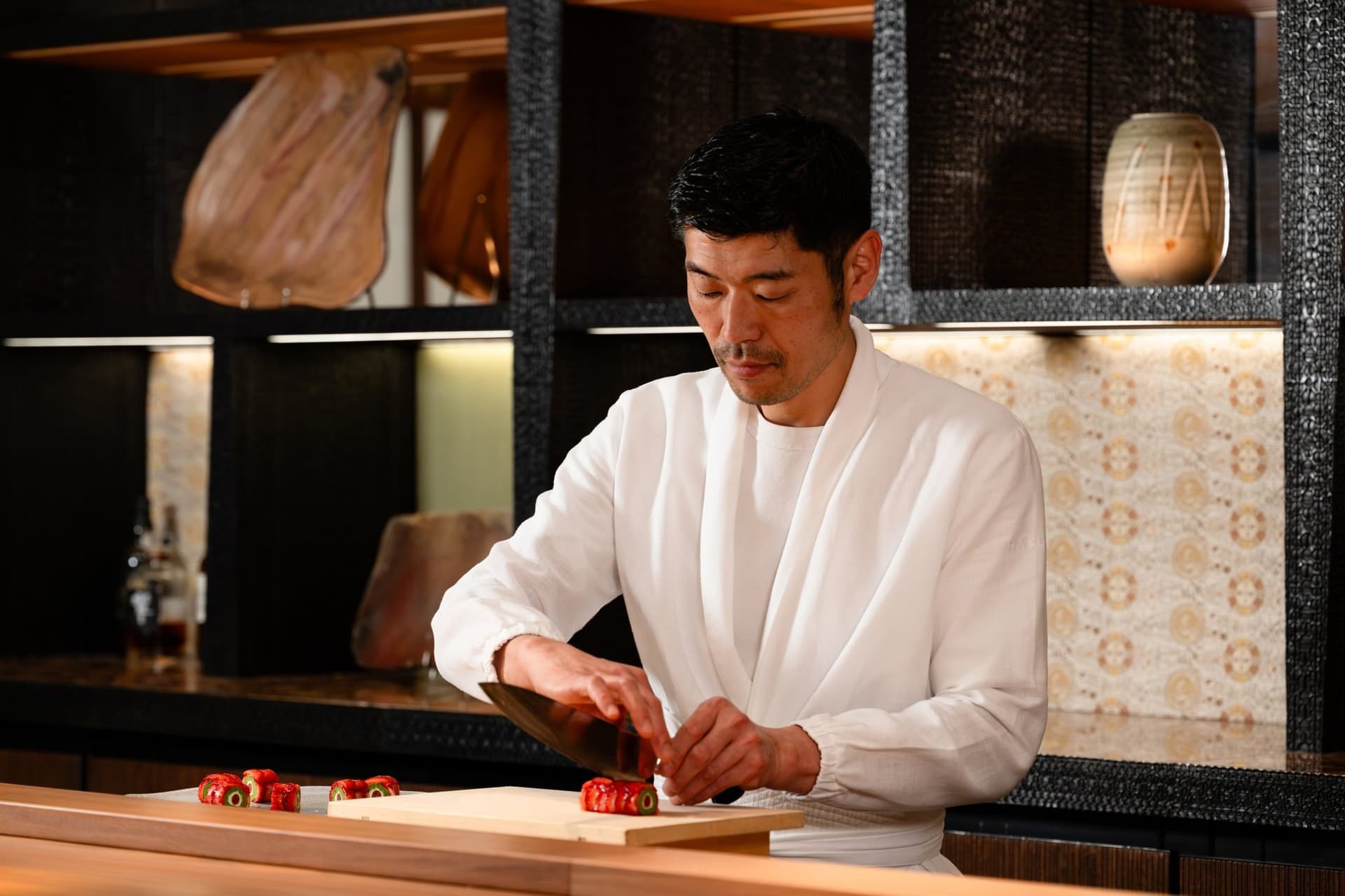 Un chef du Hakuba en veste blanche tranche un futomaki à la fraise au comptoir en bois sombre