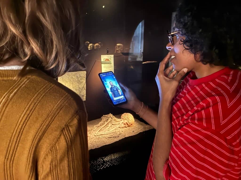 Deux visiteurs suivent l'enquête sur un téléphone devant une vitrine du Musée de l'Homme