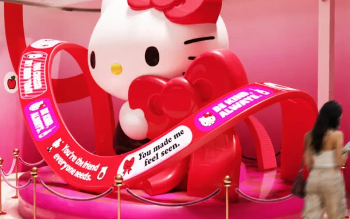 Statue géante de Hello Kitty entourée de rubans rouges, une visiteuse passe devant l'installation
