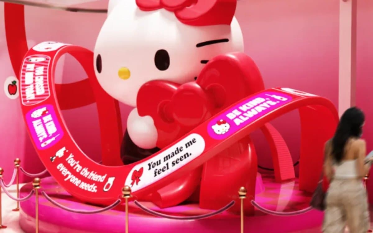 Statue géante de Hello Kitty entourée de rubans rouges, une visiteuse passe devant l'installation