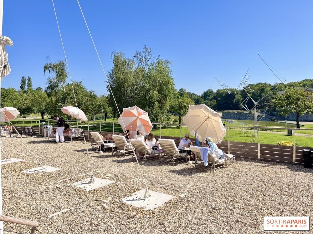 Transats et parasols sur le gravier face au lac, devant le pop-up de l'Hôtel Mahfouf