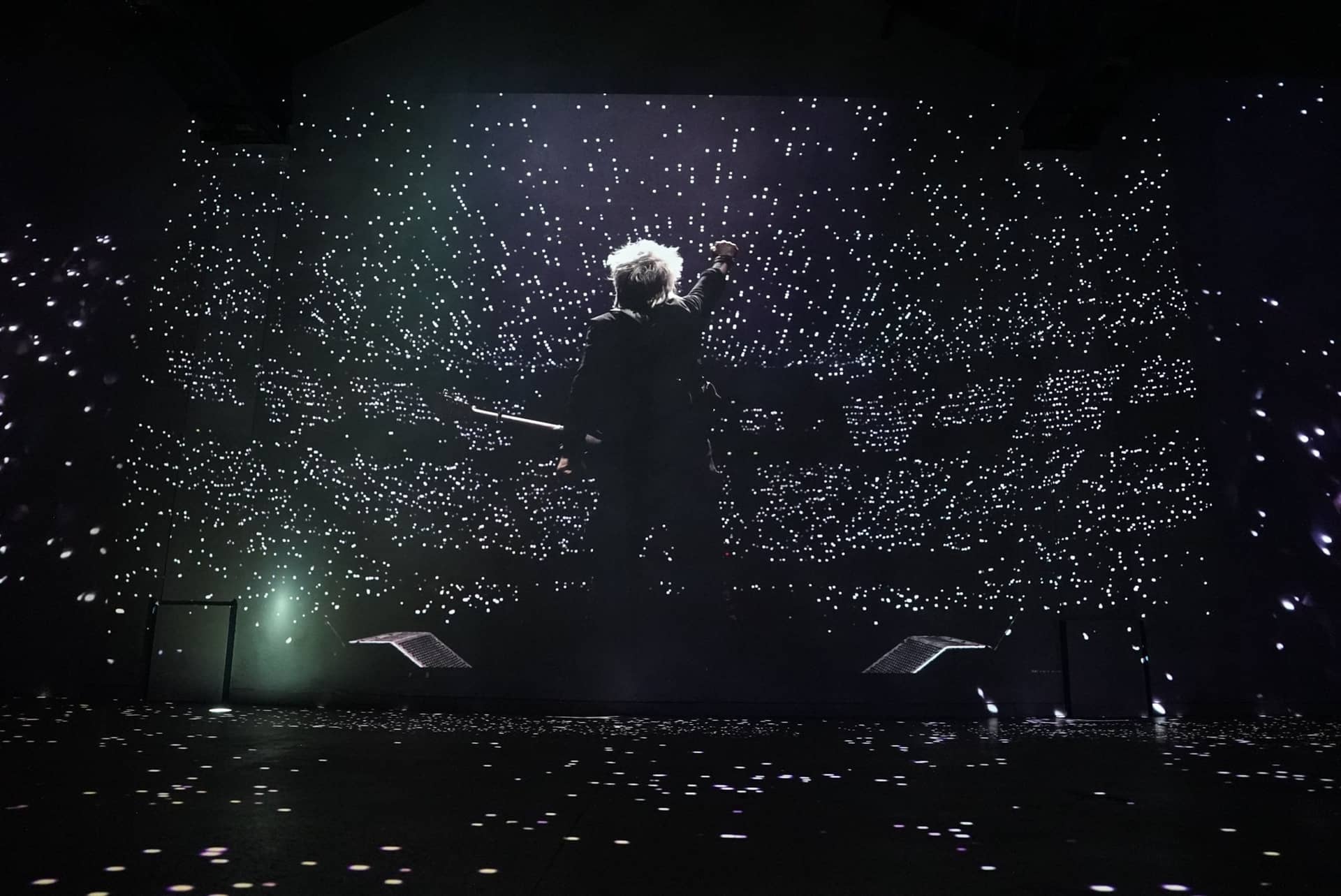 Silhouette du chanteur d'Indochine face à une salle constellée de points lumineux, projetée sur le mur de l'Atelier des Lumières
