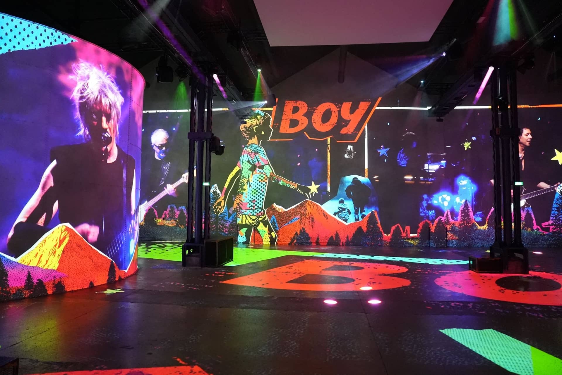La halle de l'Atelier des Lumières couverte d'images du concert d'Indochine, le mot BOY projeté en orange au sol