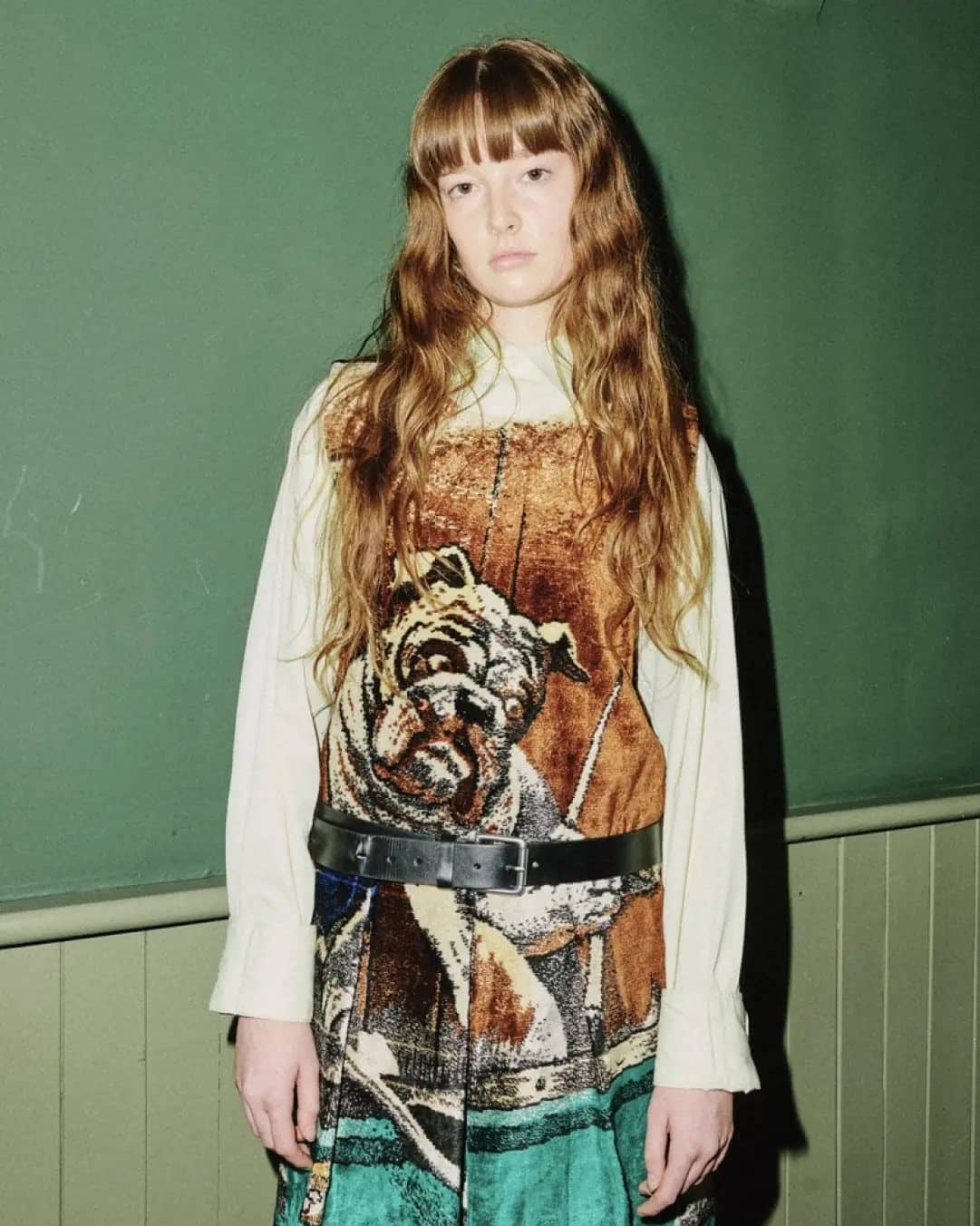 Mannequin aux cheveux longs en robe imprimée d'un tigre, ceinture en cuir, devant un mur vert