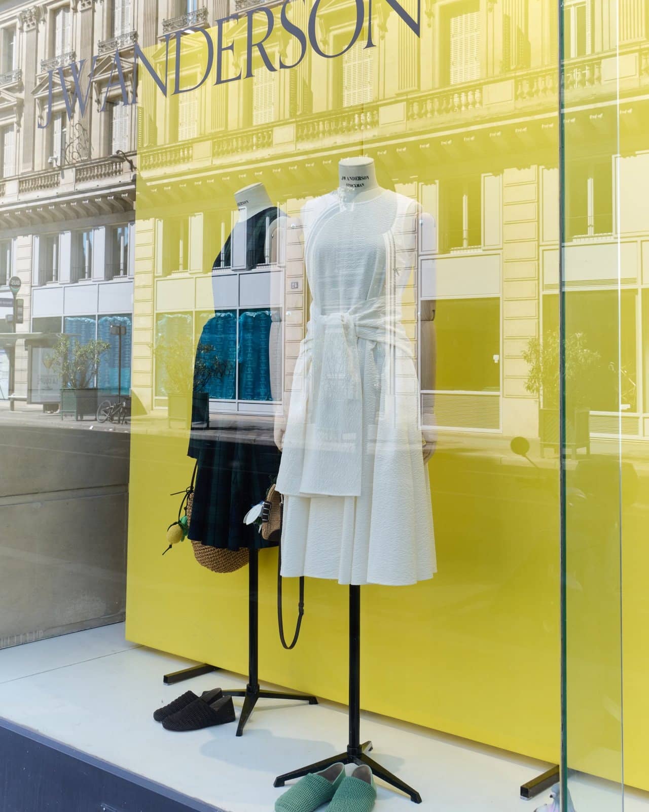 Vitrine jaune acide du pop-up JW Anderson rue du Louvre, mannequin en robe blanche vu depuis la rue