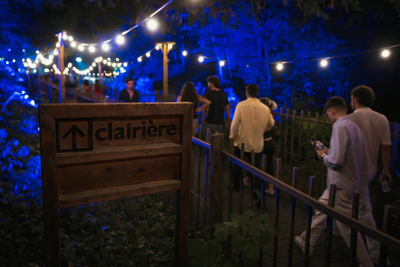 Panneau en bois gravé clairière avec une flèche, éclairé en bleu à l'entrée du site