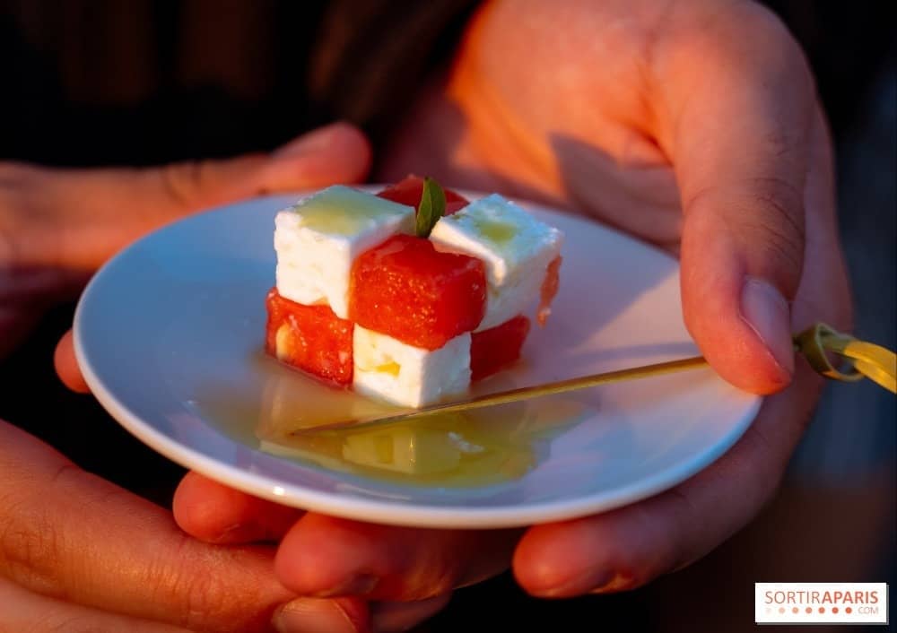 Cube de pastèque et feta à l'huile d'olive tenu au-dessus d'une assiette blanche au coucher du soleil