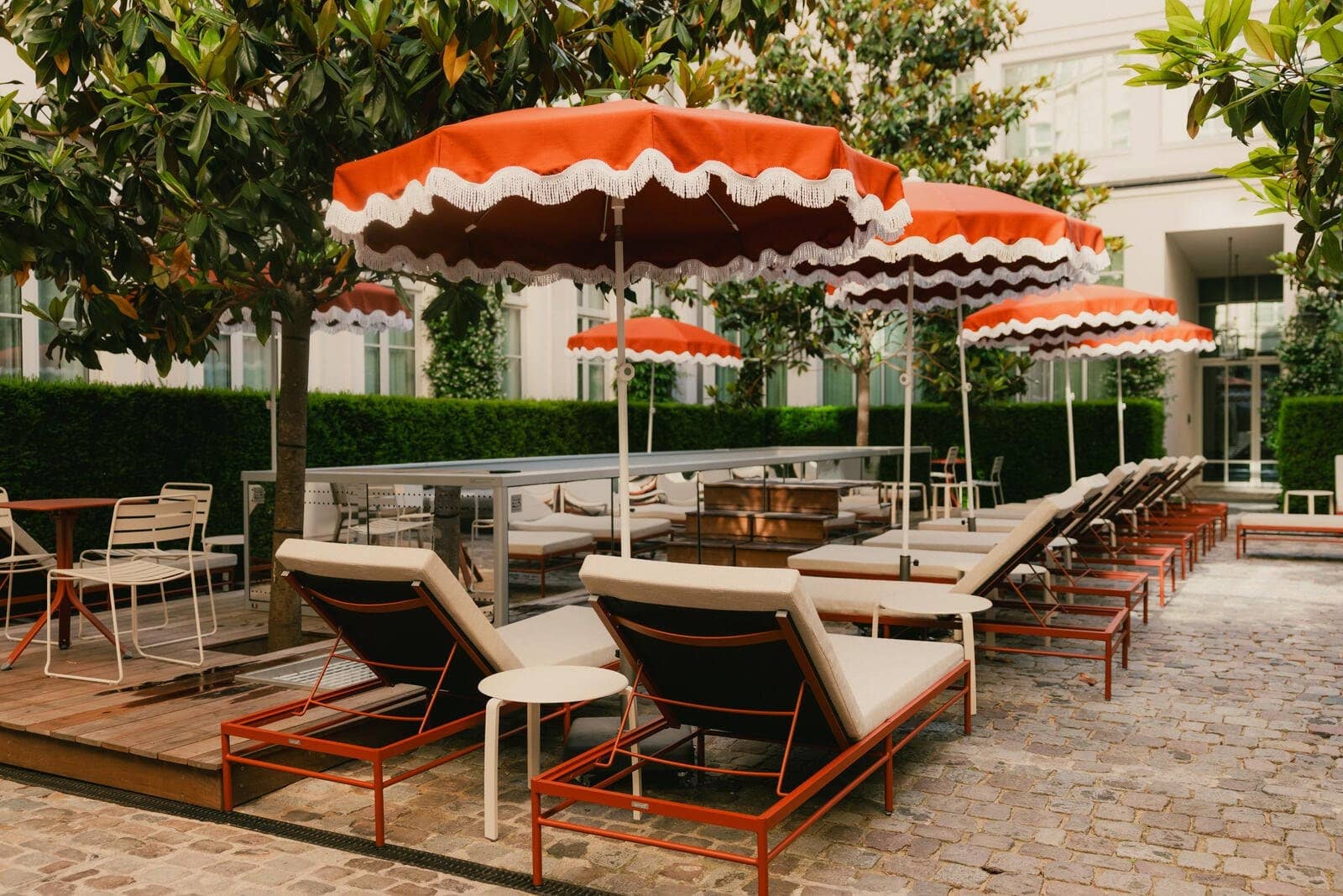 Parasols orange à festons et transats en bois alignés le long de la terrasse pavée
