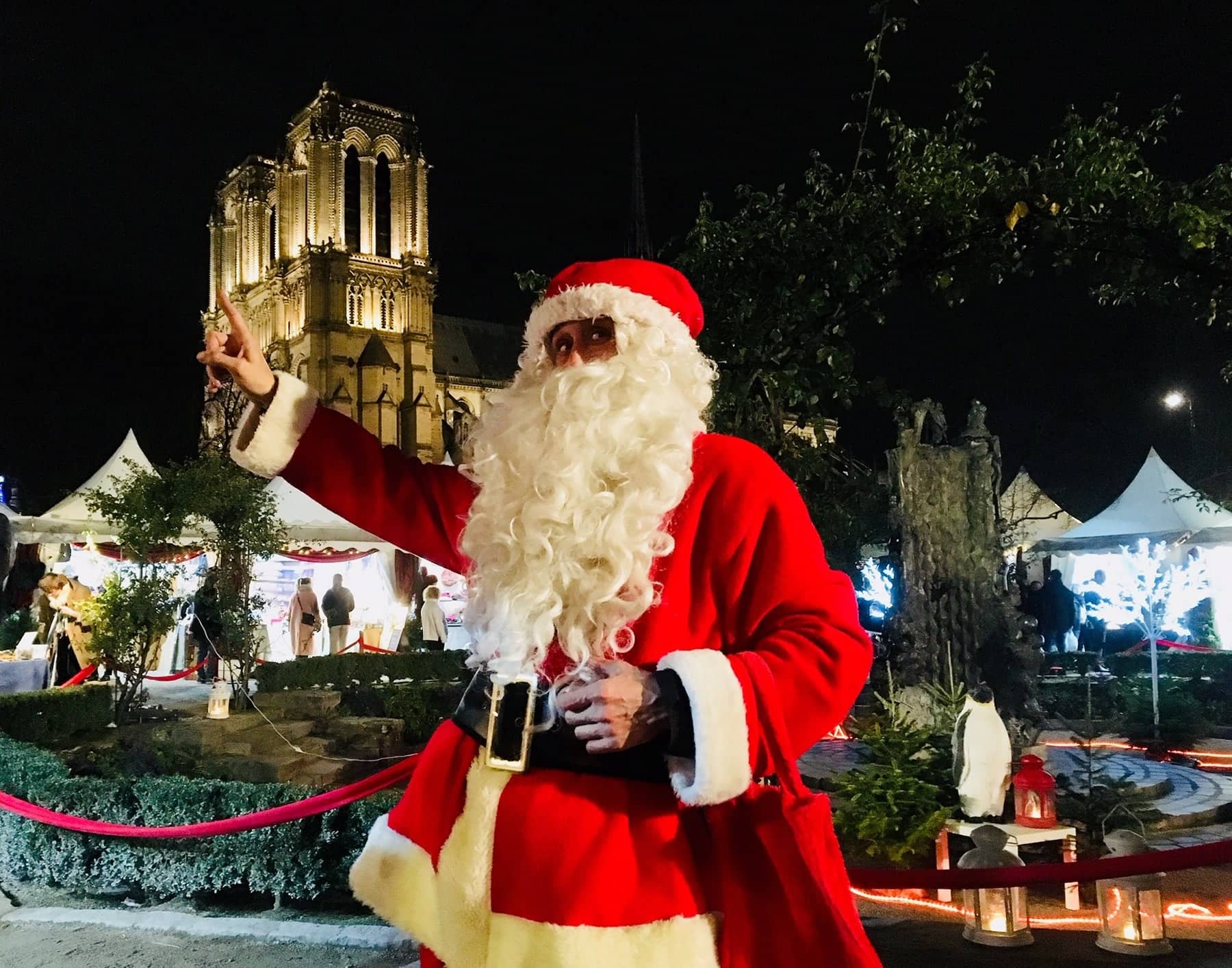 Le Père Noël devant les chalets du marché de Noël de Notre-Dame, la cathédrale illuminée au fond
