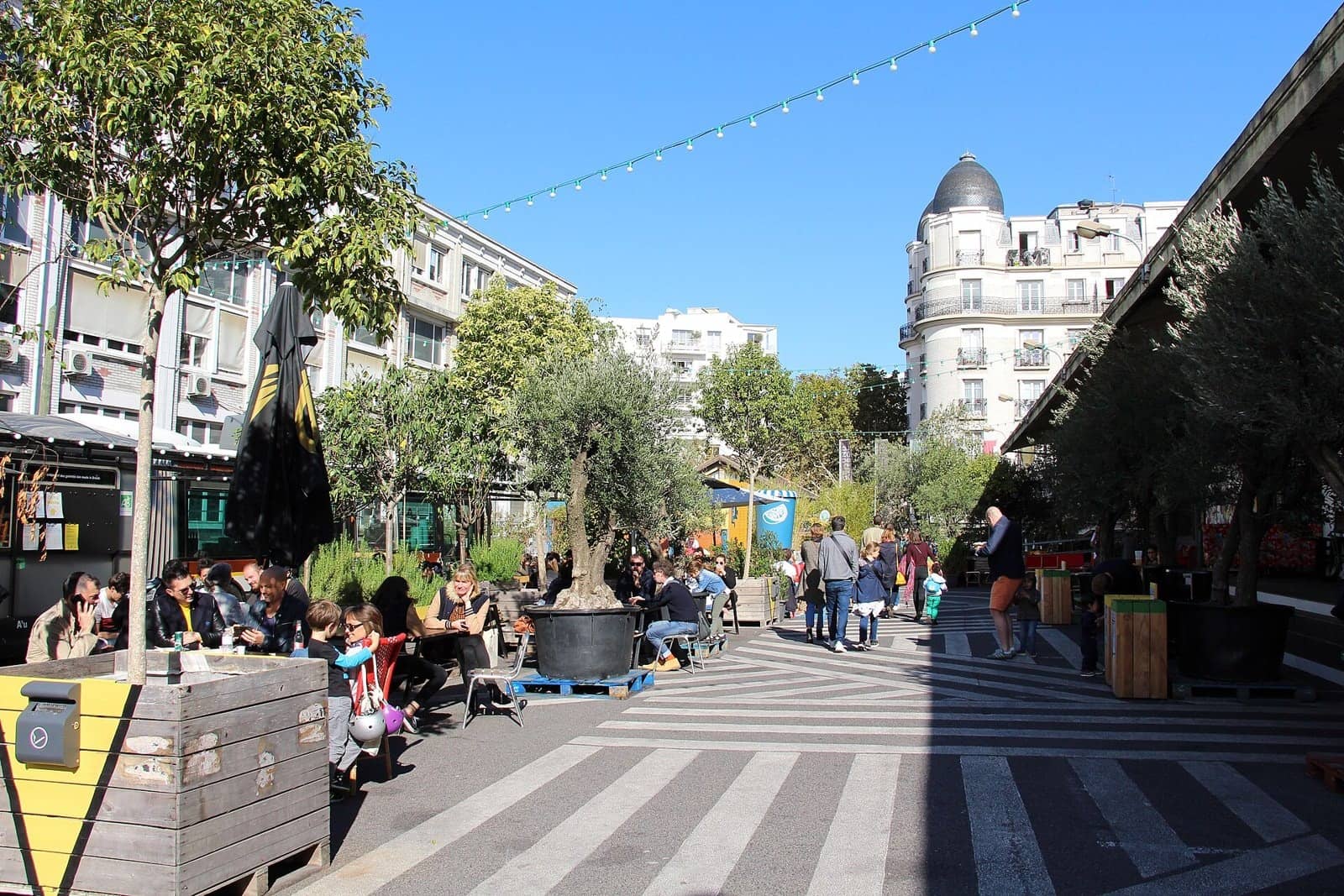 La cour de Ground Control à Paris 12e, tables en terrasse, oliviers en pots et guirlandes sous un ciel bleu