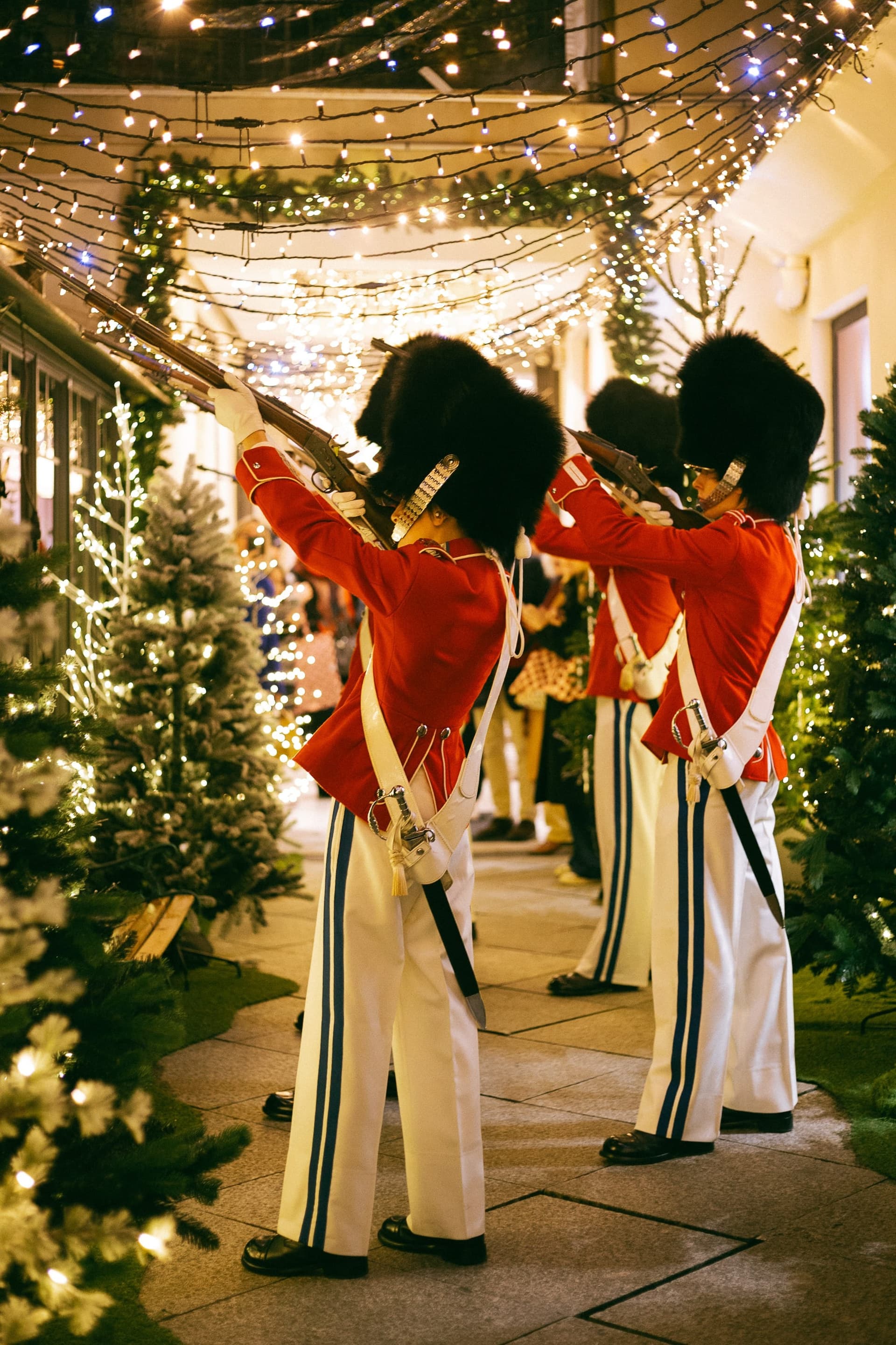 Tivoli guards in red tunics and bearskin hats among lit-up fir trees at the Maison du Danemark at Christmas