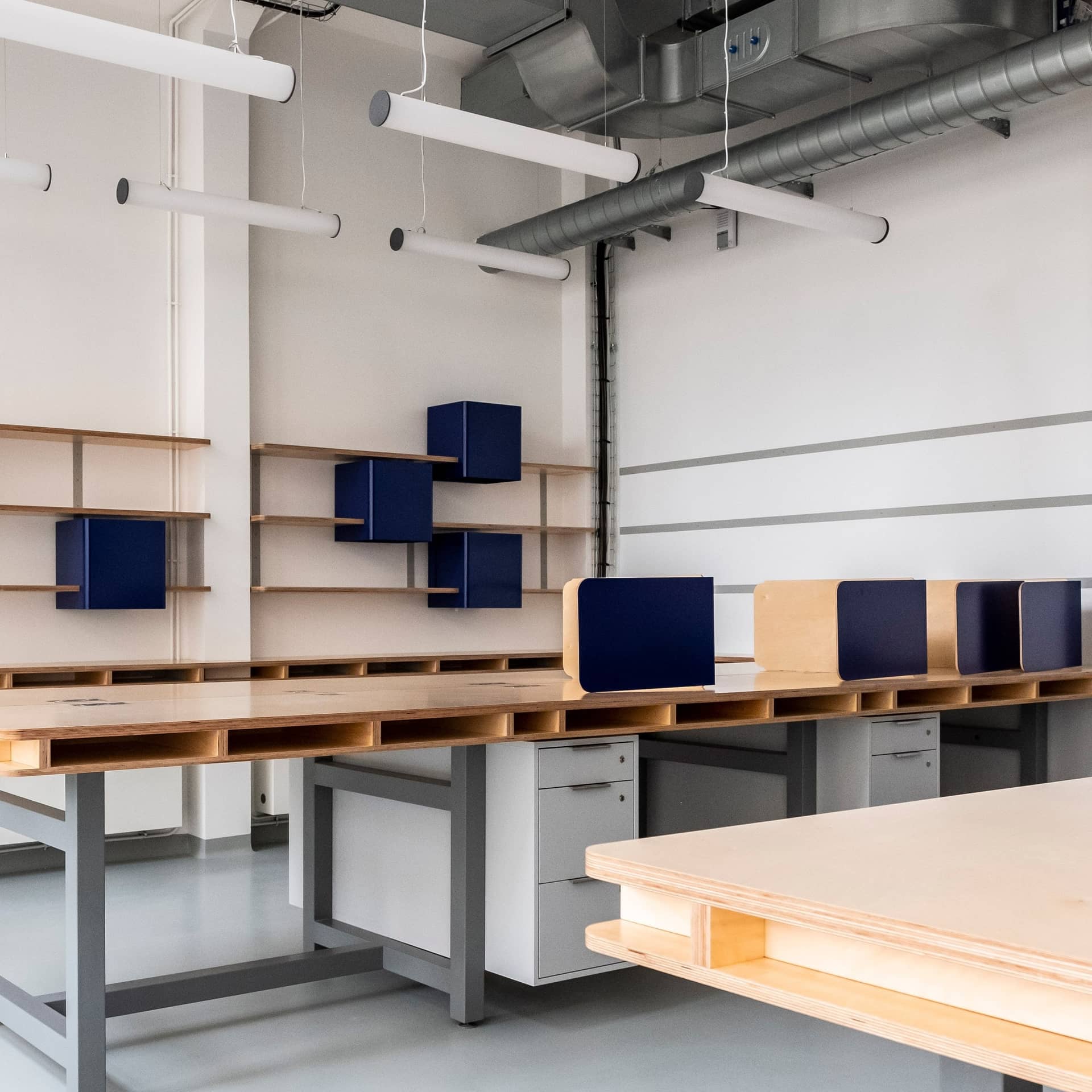 Établis en bois clair et caissons bleu nuit du MakerLab du JAD