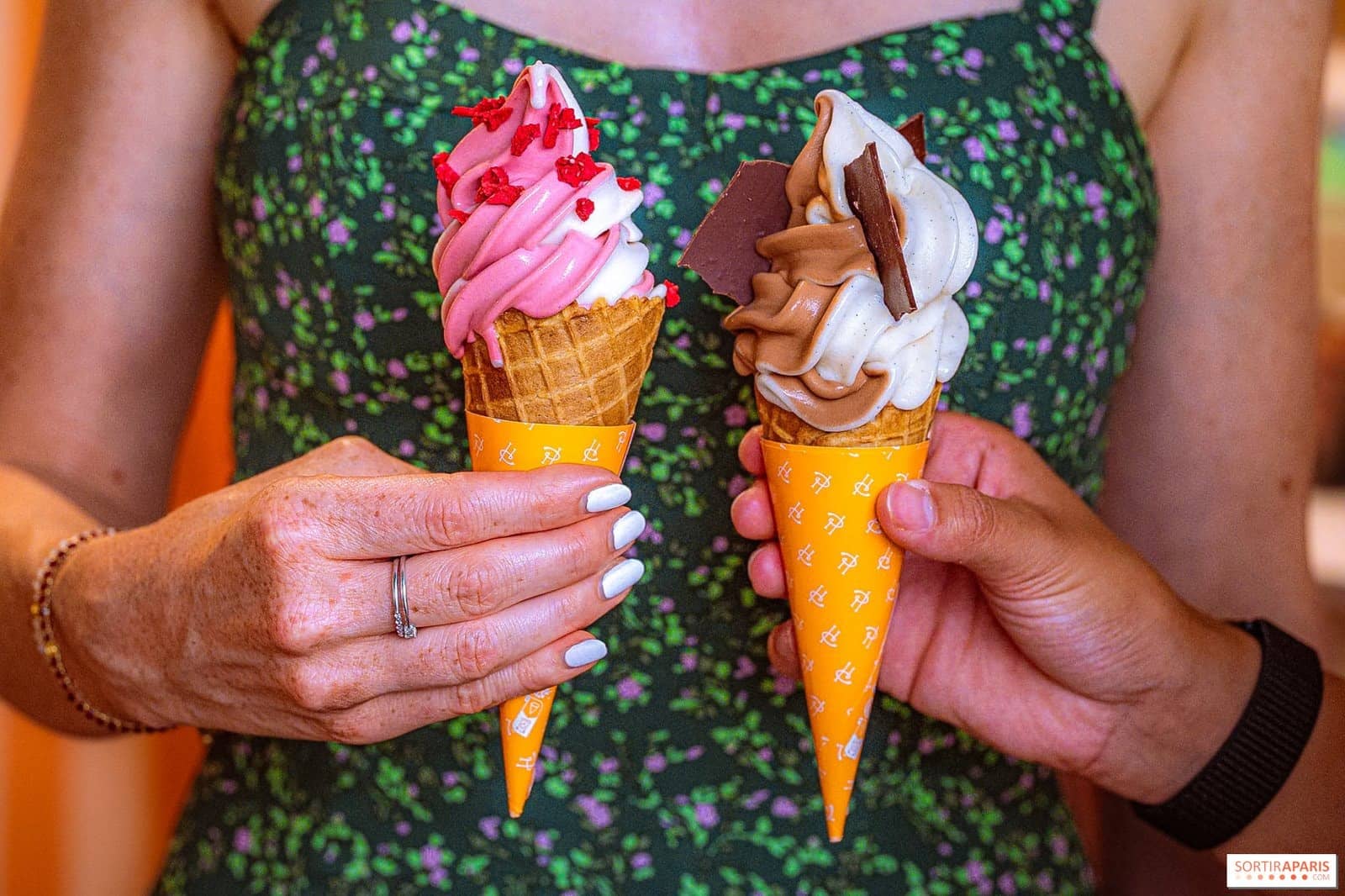 Deux cornets de glace Pierre Hermé tenus à bout de bras devant une robe fleurie verte