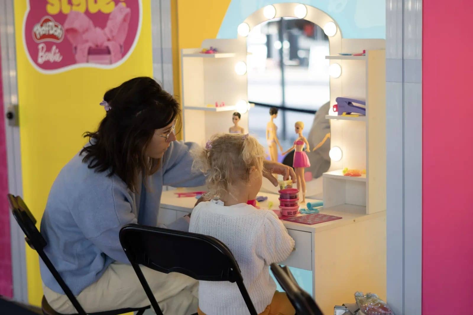 Une mère et sa petite fille jouent avec des poupées devant une coiffeuse à miroir lumineux sur un stand