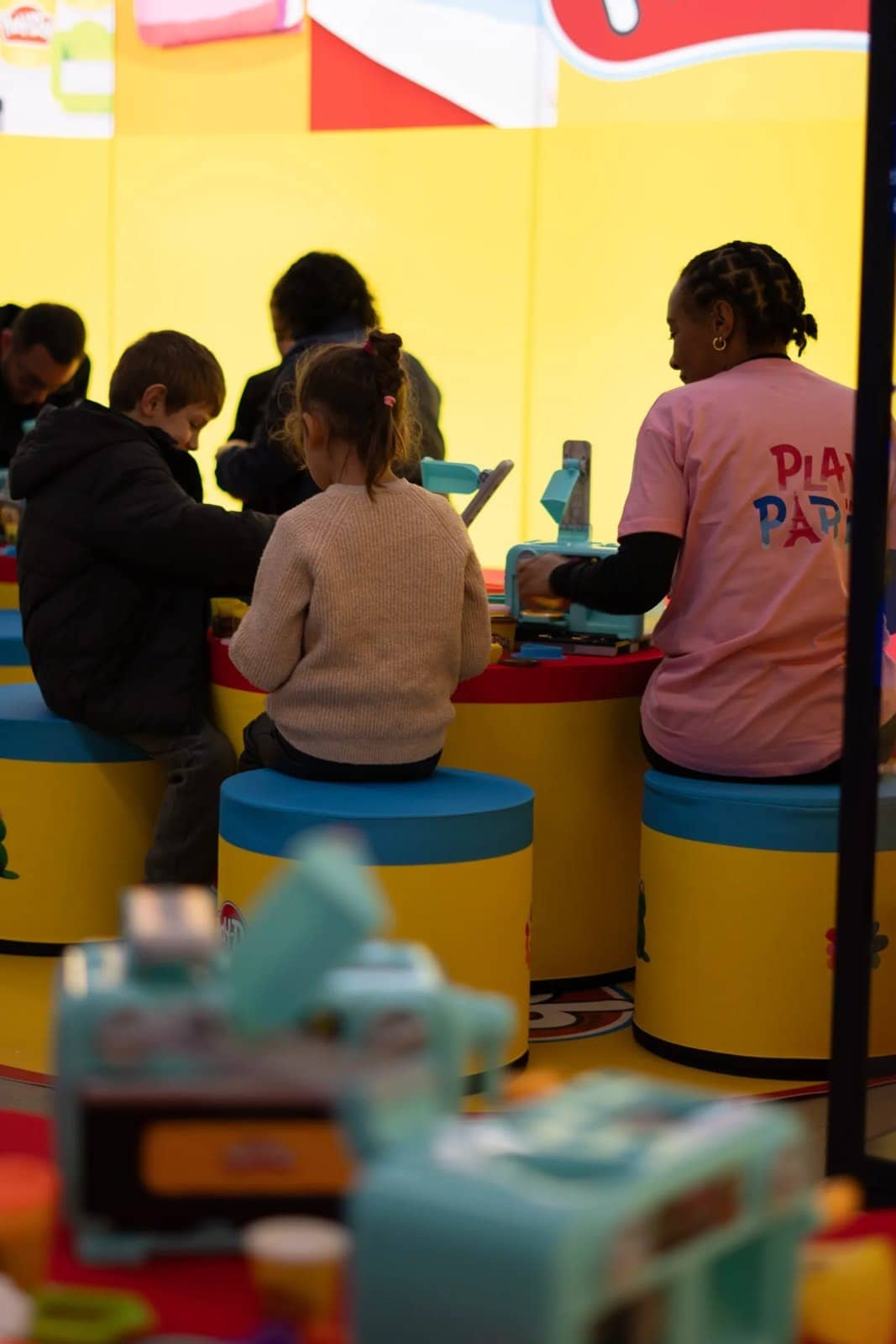 Des enfants assis sur des tabourets colorés jouent à un atelier, guidés par une animatrice en tee-shirt rose