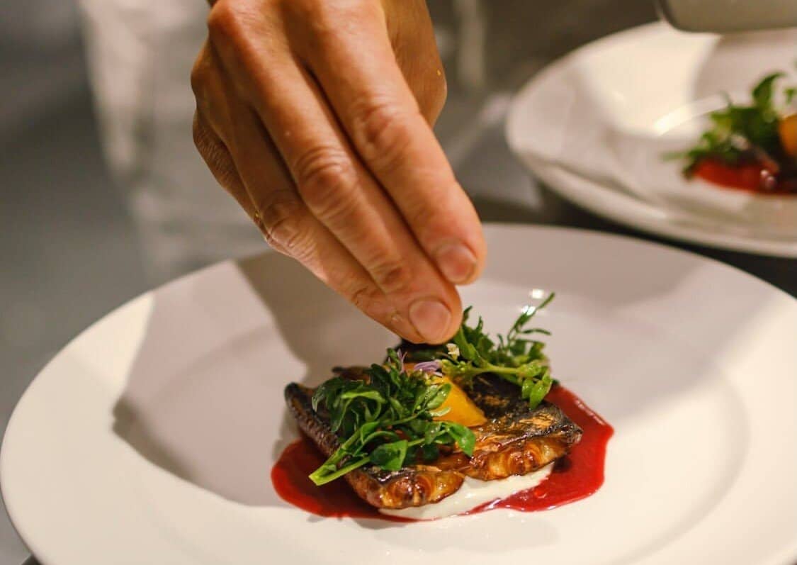 Chef Rimpei Yoshikawa's hand placing fresh herbs on a plate of grilled fish