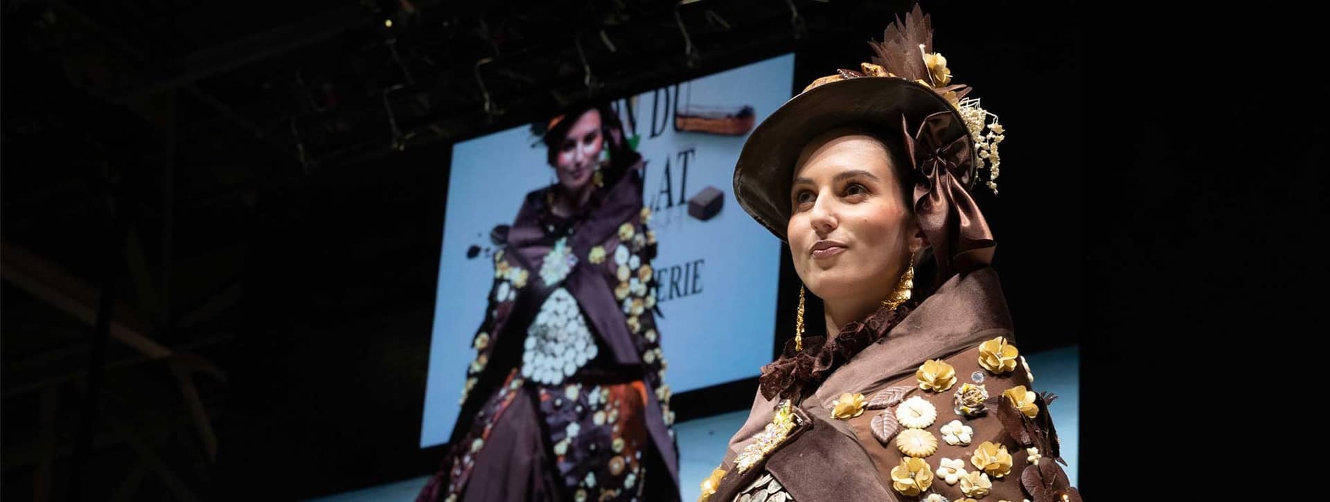 Mannequin en costume de chocolat orné de fleurs et chapeau sur la scène du défilé du Salon du Chocolat