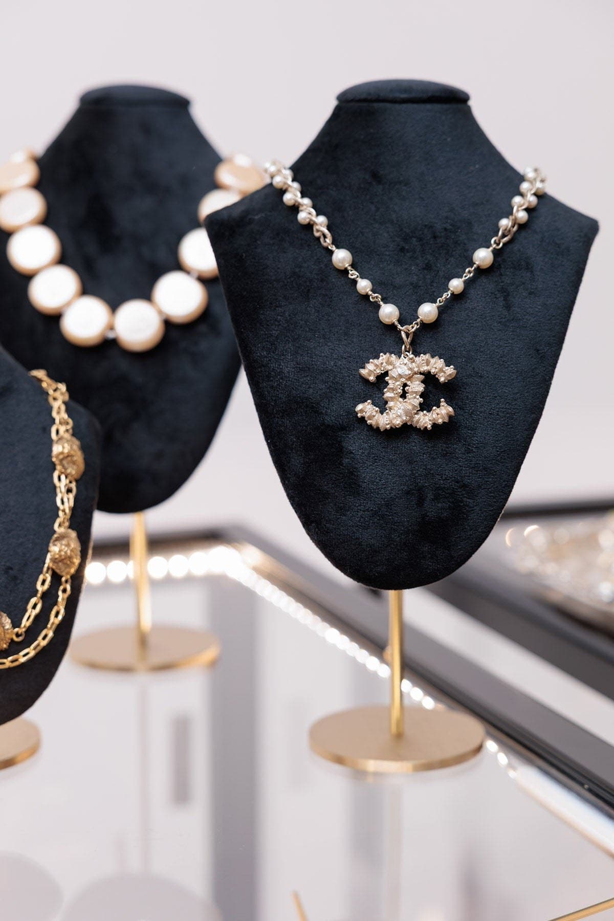 Colliers Chanel en perles et strass présentés sur des bustes de velours bleu nuit