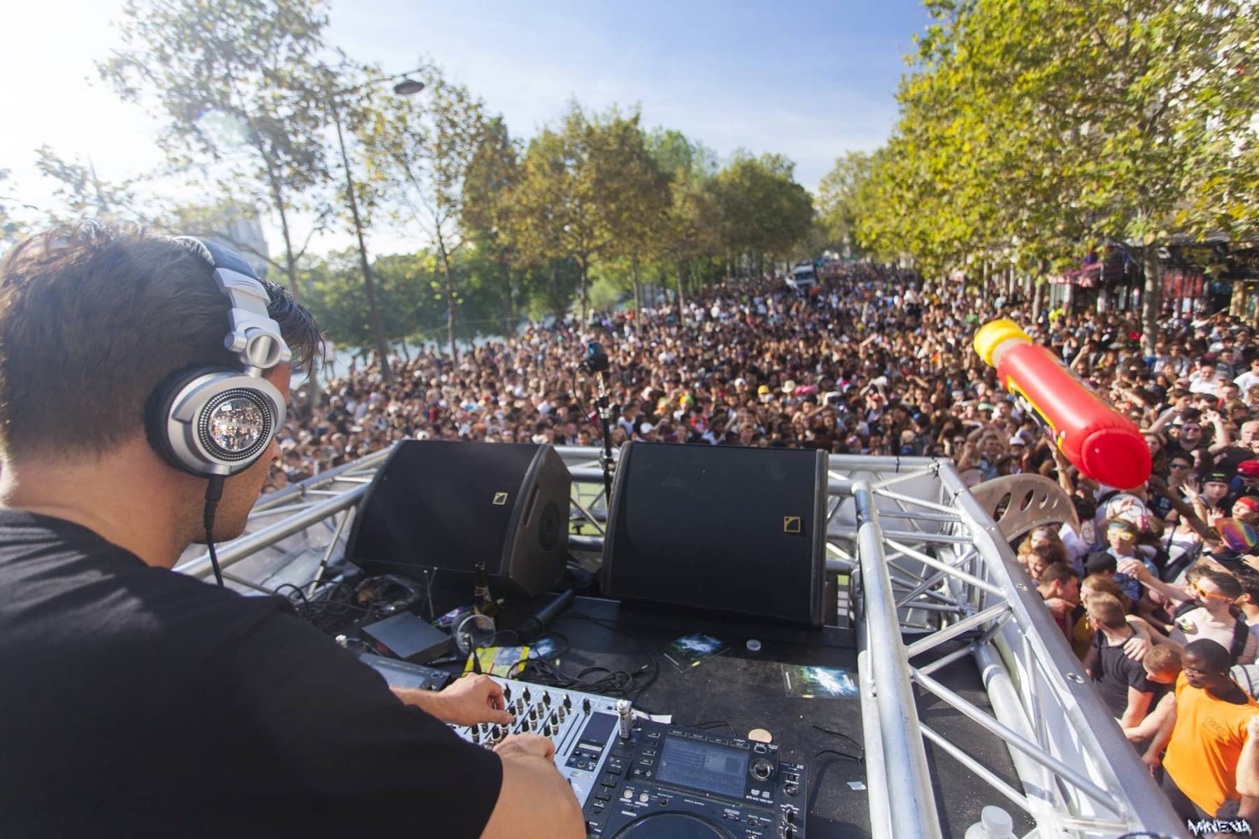 DJ aux platines sur un char de la Techno Parade, foule compacte sur le boulevard en contrebas