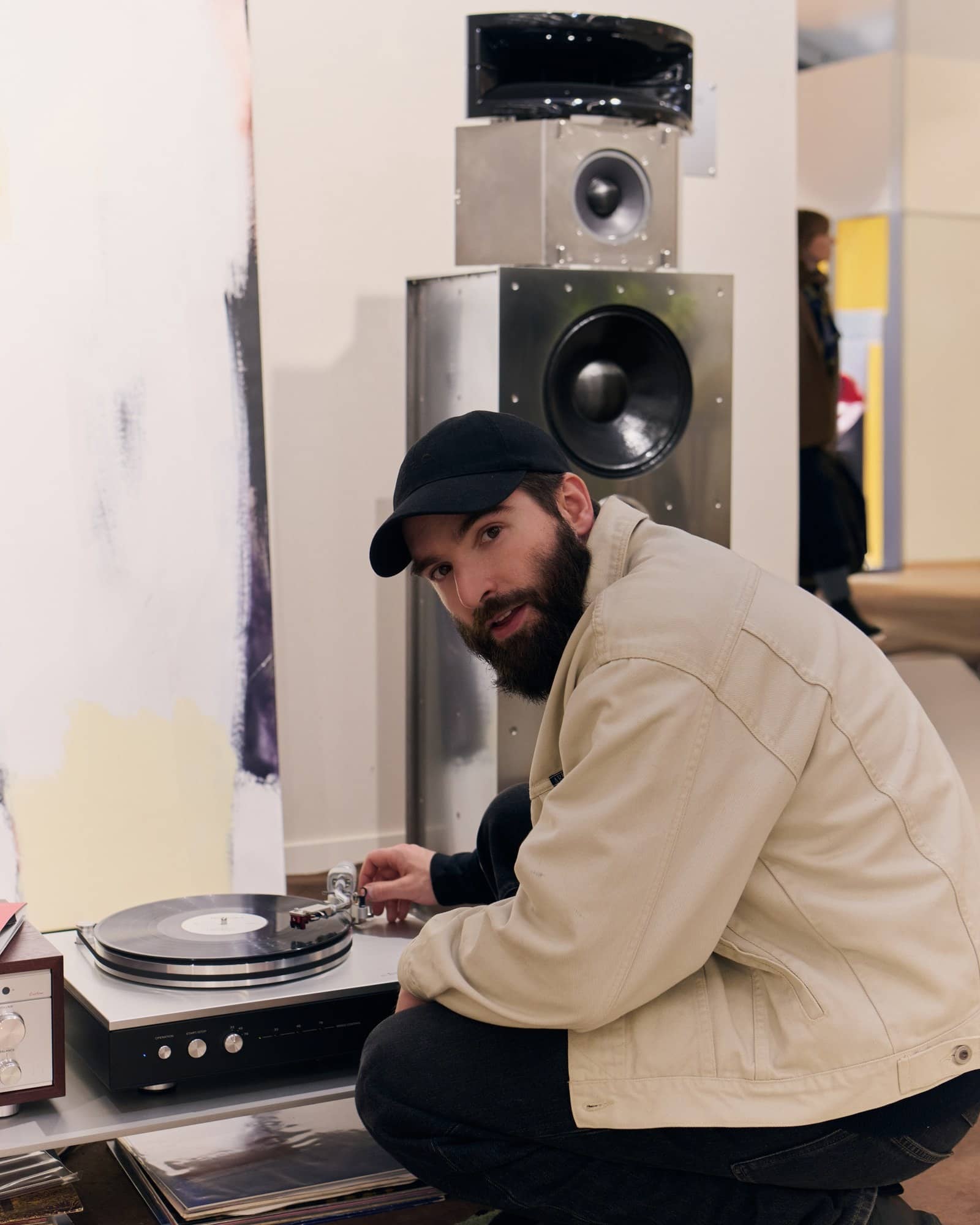 Le designer audio Matéo Garcia accroupi près d'une platine vinyle et de grandes enceintes en métal