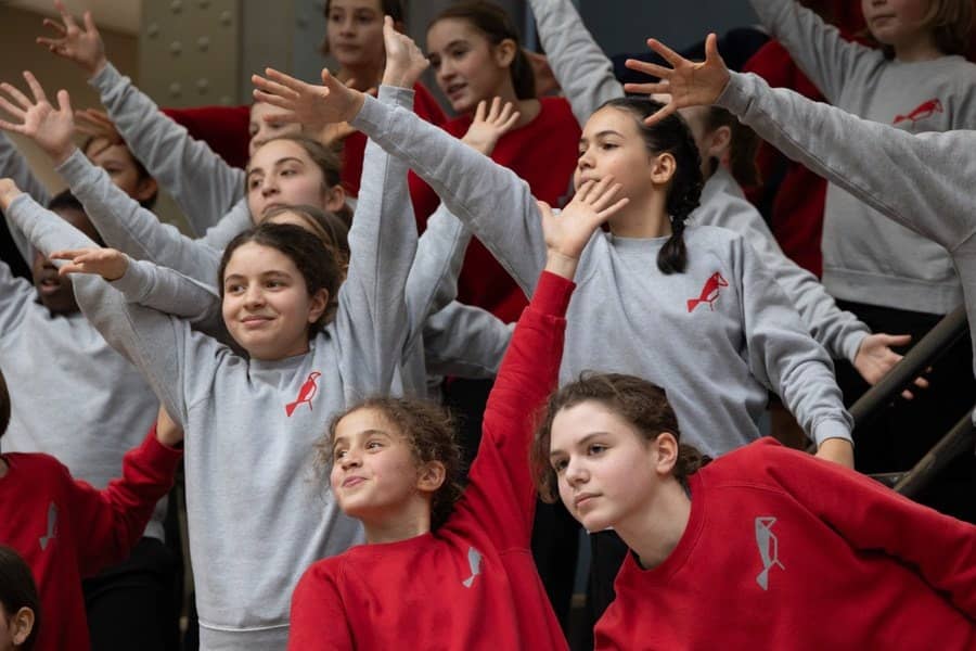 Les jeunes chanteurs de la Maîtrise populaire de l'Opéra-Comique en sweats rouges et gris, bras levés