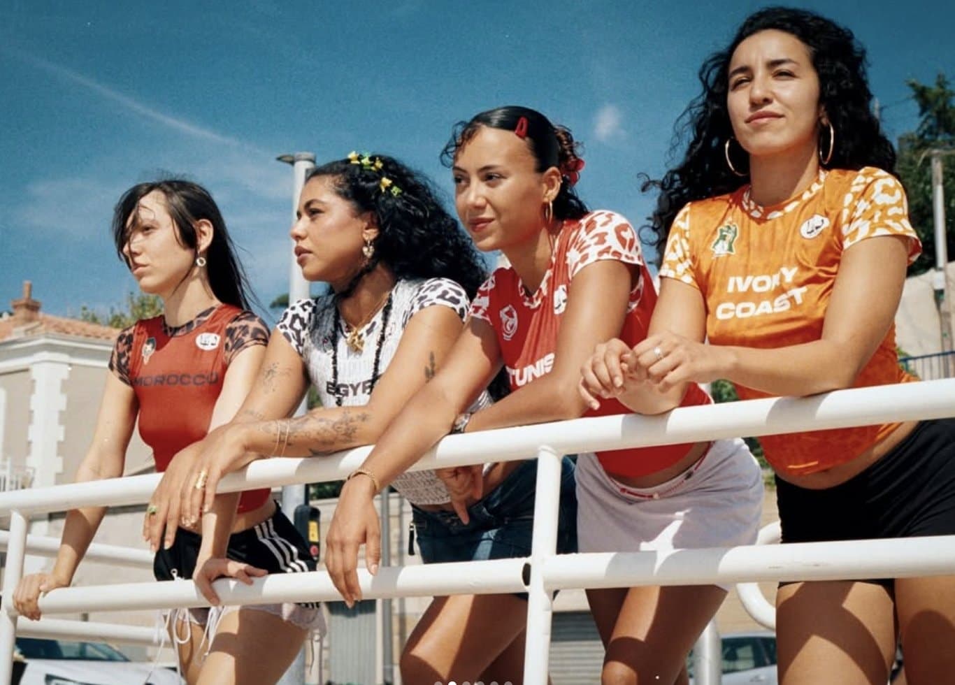 Quatre joueuses en maillots de foot recyclés par ISISDÜNYA, accoudées à une rambarde blanche au soleil